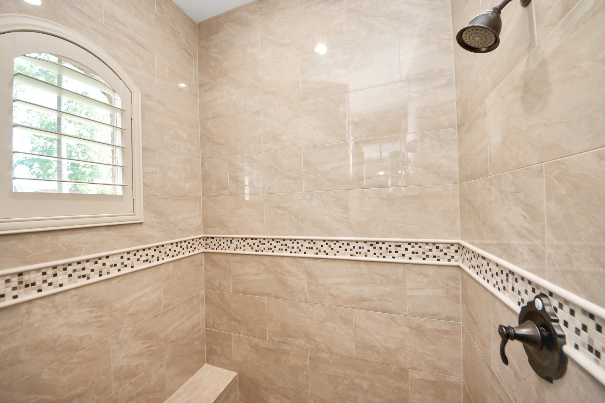 702 Fairway Oaks Conroe, TX 77302 - Photo 26 of 42 This bathroom features a
luxurious tiled shower with a
mosaic accent strip and a built
in bench. It includes a modern
showerhead and a window with
plantation shutters for natural
light