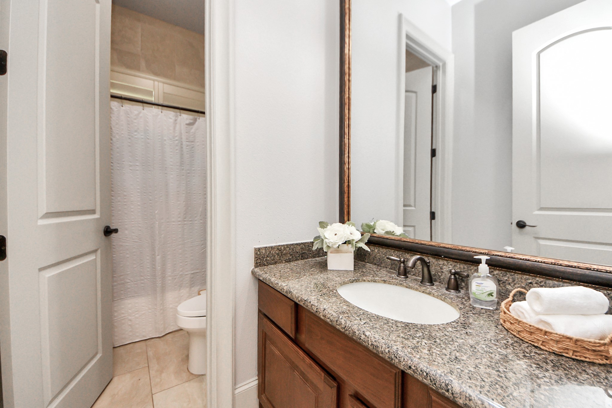 702 Fairway Oaks Conroe, TX 77302 - Photo 28 of 42 Bathroom featuring a
granite countertop with an
undermount sink, elegant
fixtures, and a large mirror. The
shower area is separated by a
curtain, and the space is
accented with fresh flowers and
neatly arranged towels.