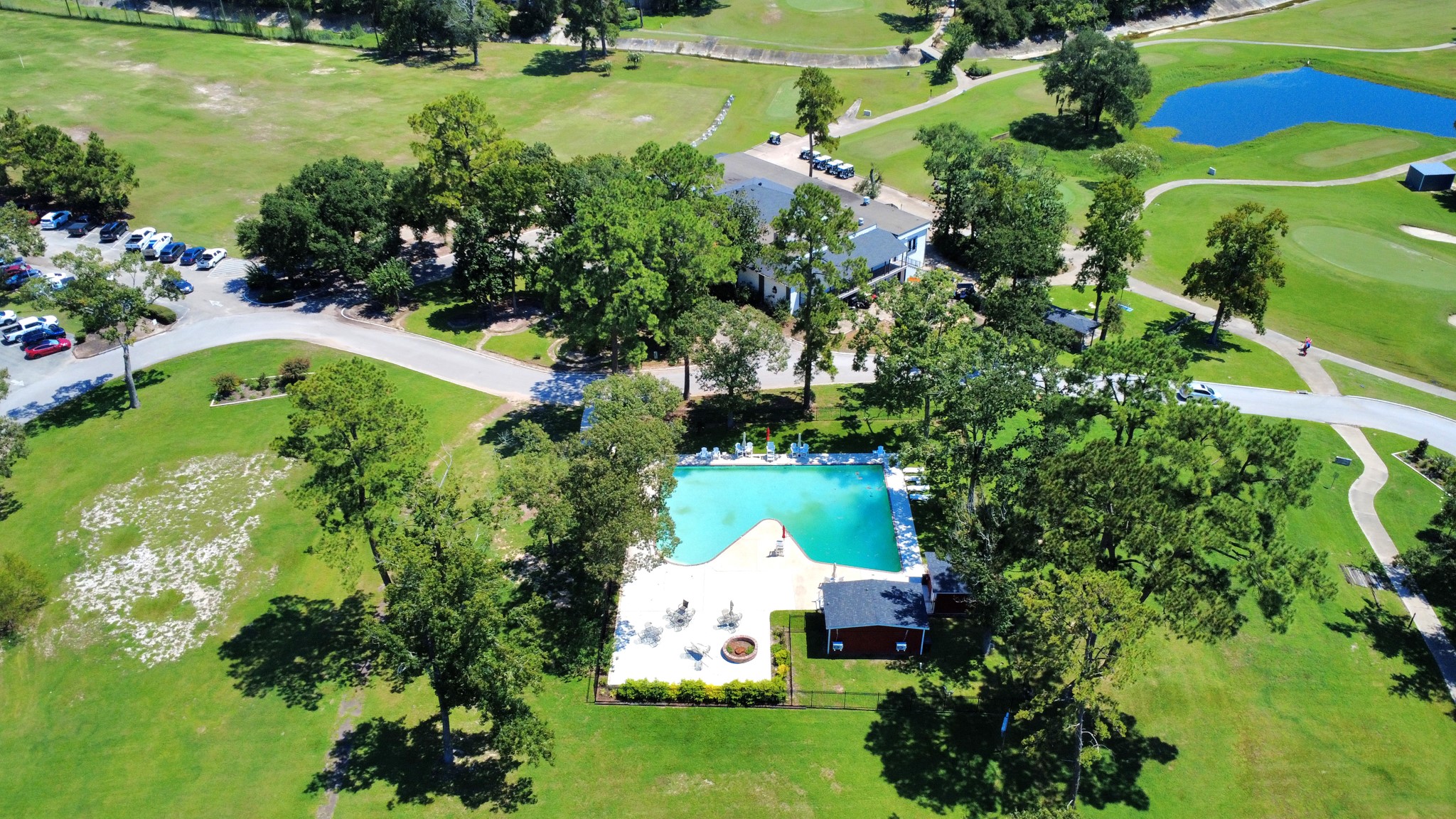 702 Fairway Oaks Conroe, TX 77302 - Photo 38 of 42 A picturesque property
featuring a large neighborhood
pool surrounded by lush
greenery and mature trees.
Nearby, a clubhouse and ample
parking are visible, set against
a backdrop of expansive green
spaces and a small pond,
offering a serene and inviting
environment