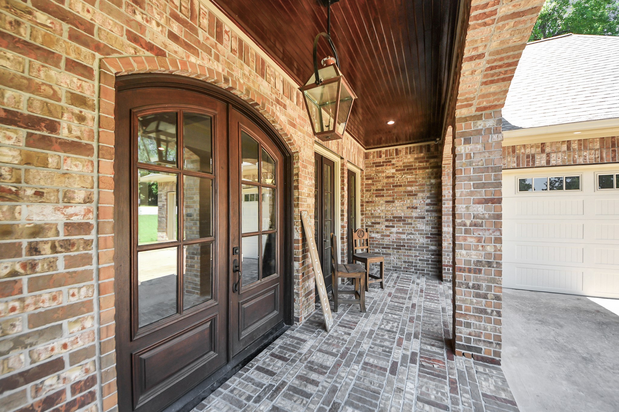 702 Fairway Oaks Conroe, TX 77302 - Photo 5 of 42 A charming, brick-clad front
porch with elegant arched
double doors and a covered
entryway. The space is
accented by a rustic lantern
style light fixture and a cozy
seating area, offering a warm
and inviting entrance to the
home.