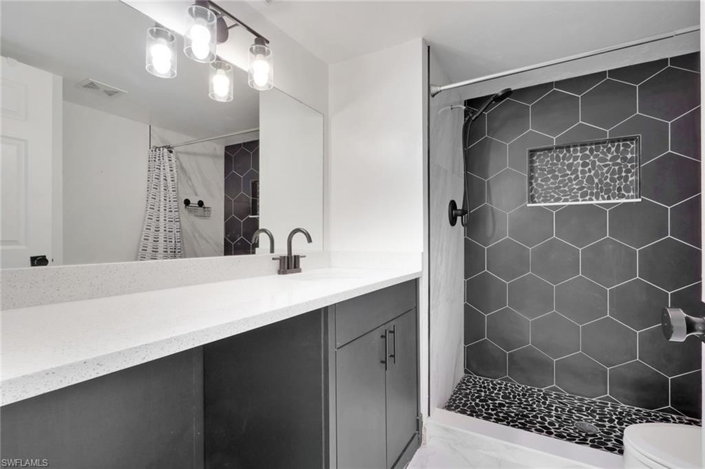 146 Cypress Way East, Unit 807 Naples, FL 34110 - Photo 18 of 27 a bathroom with a sink a mirror a vanity and a shower