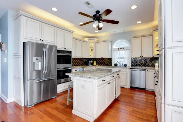 a kitchen with stainless steel appliances kitchen island granite countertop a refrigerator a stove a sink and white cabinets with wooden floor