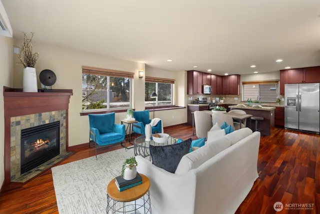a living room with stainless steel appliances furniture a fireplace a rug and a view of kitchen