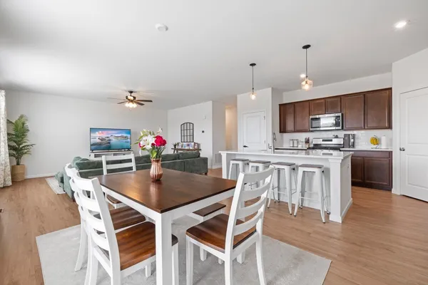 a kitchen with stainless steel appliances granite countertop a stove top oven a refrigerator a kitchen island a dining table and chairs with wooden floor