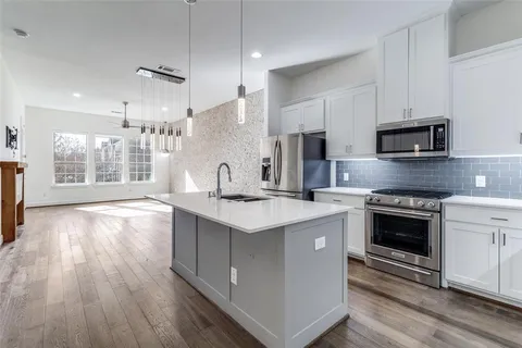 a kitchen with stainless steel appliances granite countertop a stove top oven a sink dishwasher and a refrigerator with wooden floors