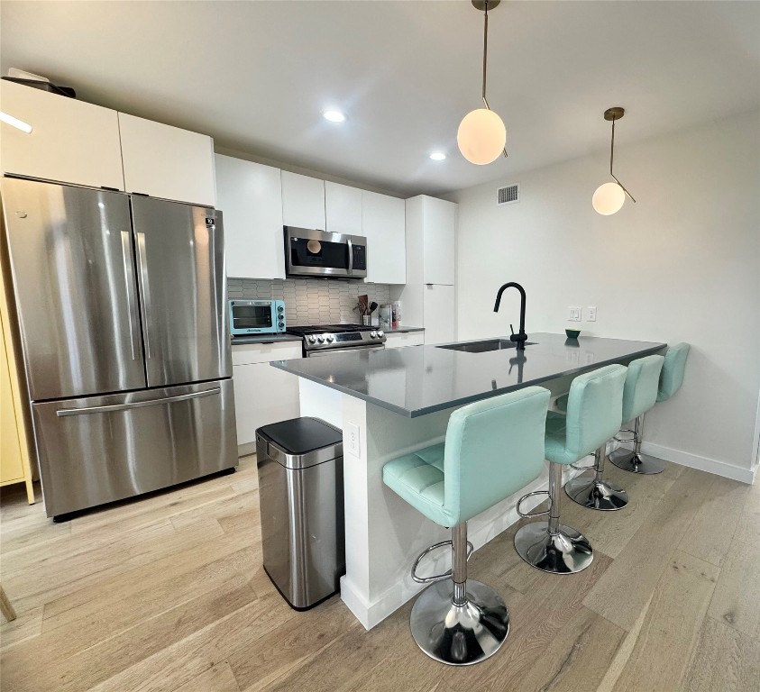 400 East 30th Street, Unit 101 Austin, TX 78705 - Photo 10 of 27 Kitchen with appliances with stainless steel finishes, a breakfast bar, pendant lighting, a peninsula, and tasteful backsplash