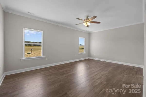 a view of an empty room with wooden floor and a ceiling fan