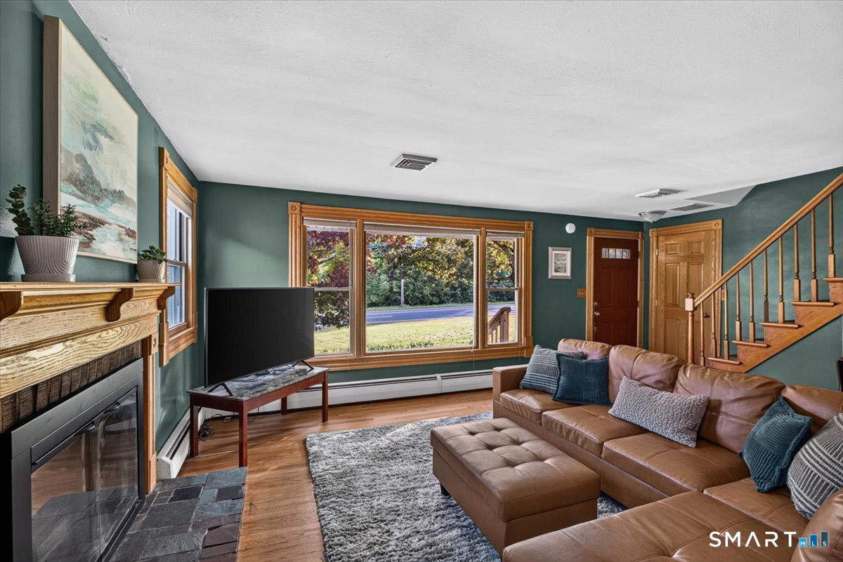 121 Hartford Road Simsbury, CT 06070 - Photo 4 of 31 Warm and inviting living room featuring hardwood floors, a wood-burning fireplace, and an oversized picture window that fills the space with natural light.