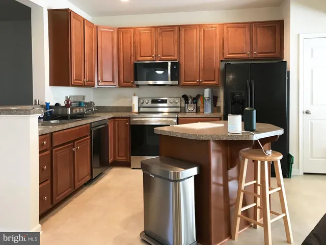 a kitchen with stainless steel appliances granite countertop a stove top oven a sink dishwasher and a refrigerator with wooden cabinets