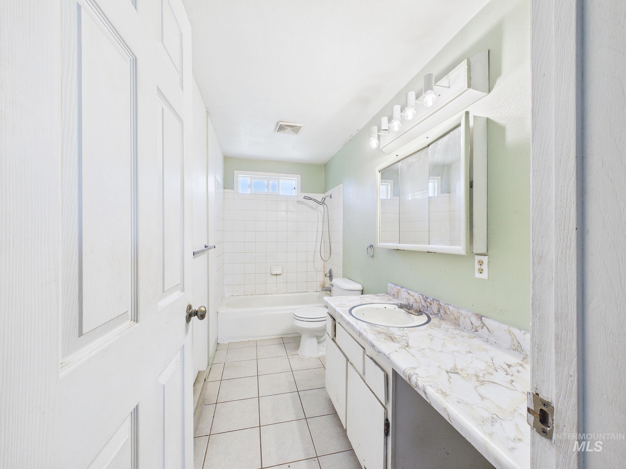 1527 North Plaza Road Emmett, ID 83617 - Photo 26 of 33 Bathroom featuring a white tiled floor, a full bathtub with white subway tile surround, a built-in vanity with a white countertop and integrated sink, a wall-mounted medicine cabinet, and a multi-bulb vanity light fixture