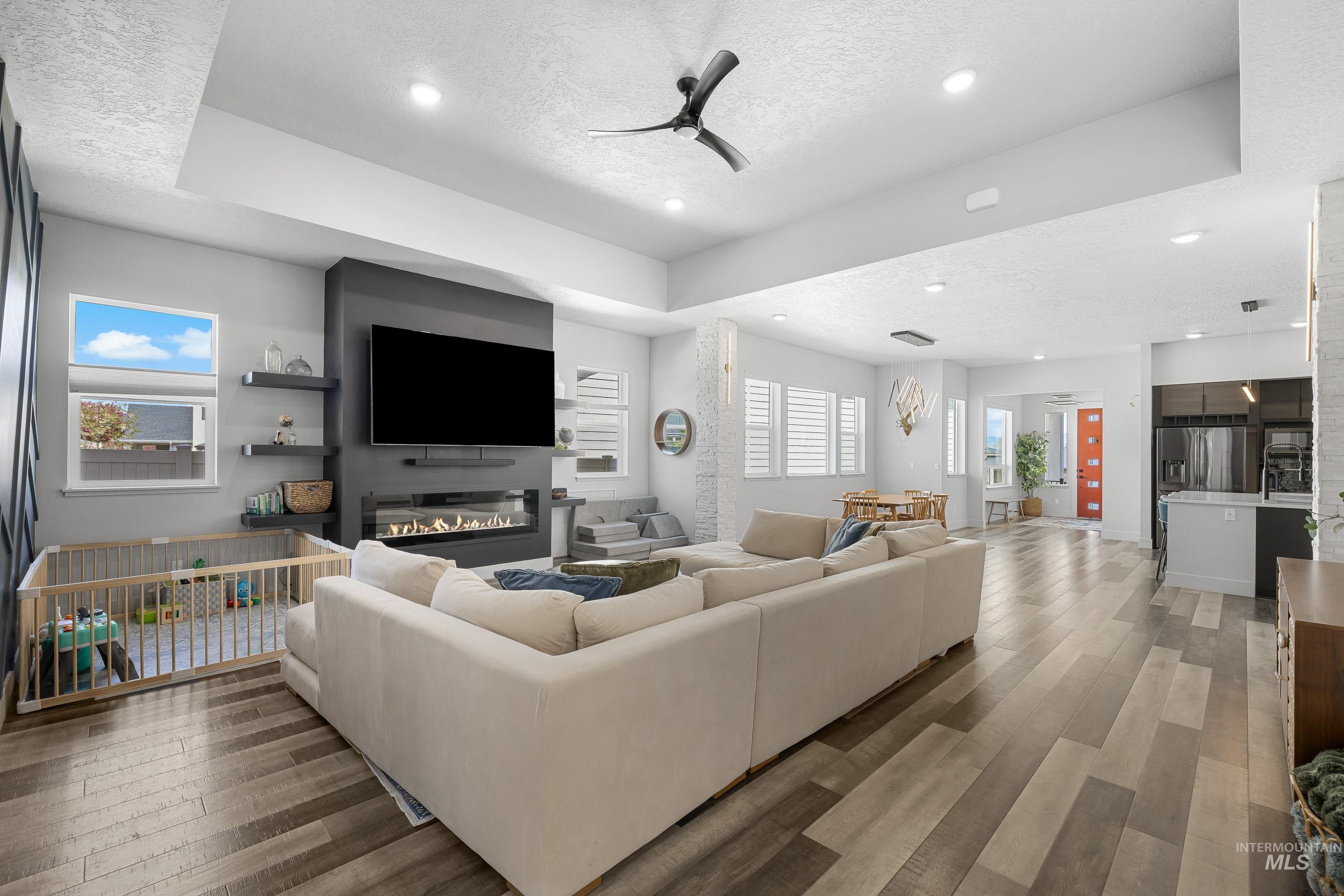 3483 South Grenze Way Meridian, ID 83642 - Photo 11 of 30 Living room featuring a ceiling fan, light wood finished floors, a textured ceiling, a tray ceiling, and a glass covered fireplace