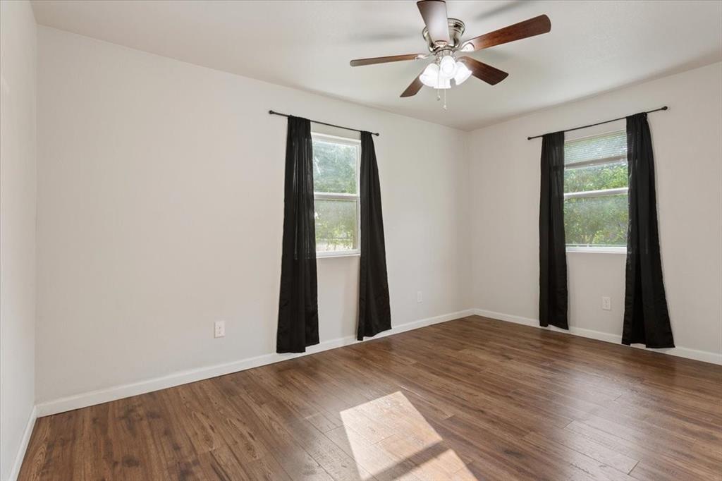 3109 North 20th Street Waco, TX 76708 - Photo 15 of 24 Room featuring two windows with dark curtains, wood-finish flooring, white walls, and a ceiling fan with integrated lighting