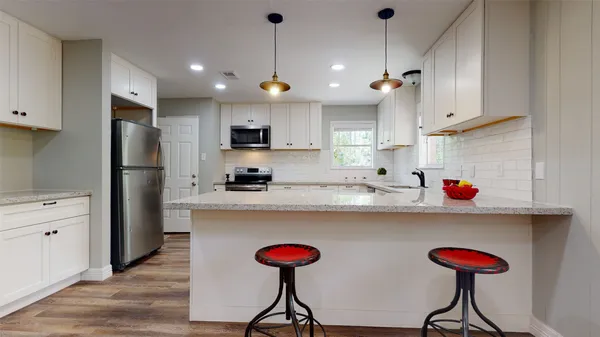 a kitchen with stainless steel appliances granite countertop a dining table chairs refrigerator and sink
