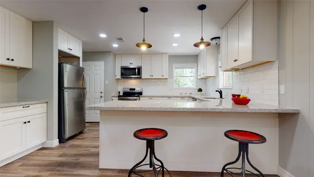 a kitchen with stainless steel appliances granite countertop a dining table chairs refrigerator and sink