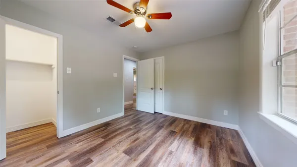 an empty room with wooden floor a ceiling fan and windows