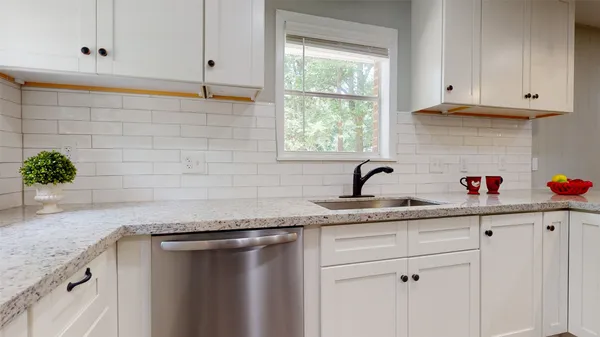 a sink with granite countertop white cabinets and a window