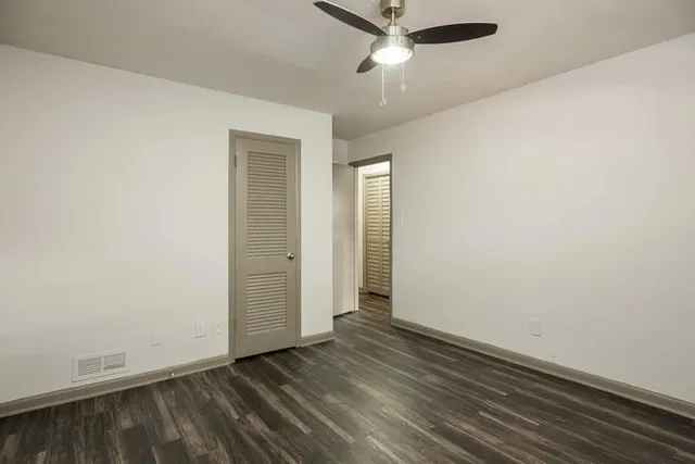 an empty room with wooden floor closet and windows