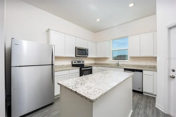 a kitchen with granite countertop a refrigerator a sink a stove a microwave and island