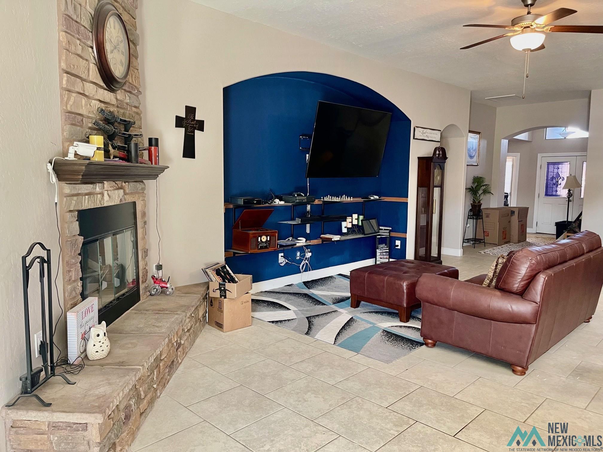 Living room with light tile patterned floors, a fireplace, arched walkways, and ceiling fan