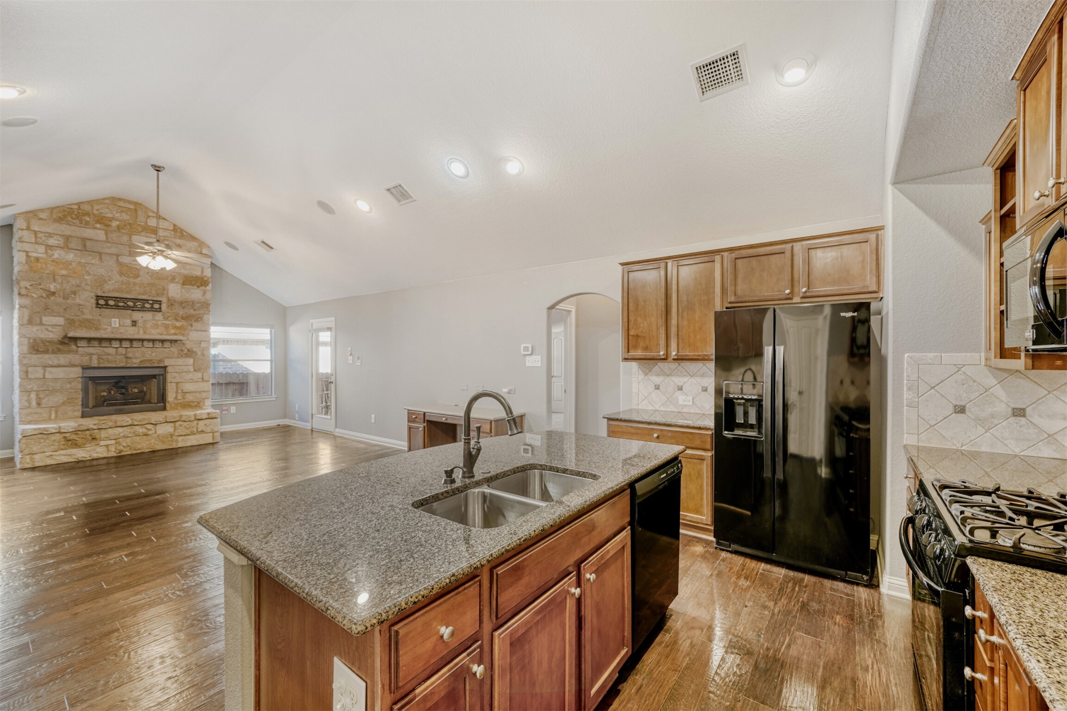2431 Santa Barbara Loop Round Rock, TX 78665 - Photo 12 of 34 Kitchen featuring black appliances, decorative backsplash, a kitchen island with sink, arched walkways, and dark wood-style floors
