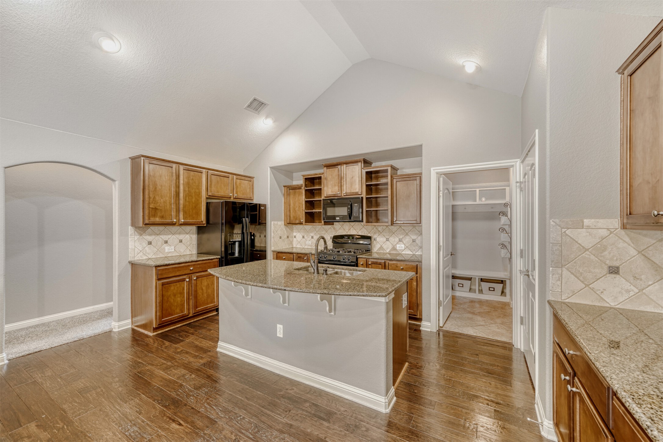 2431 Santa Barbara Loop Round Rock, TX 78665 - Photo 13 of 34 Kitchen featuring tasteful backsplash, brown cabinets, open shelves, a kitchen island with sink, and light stone countertops