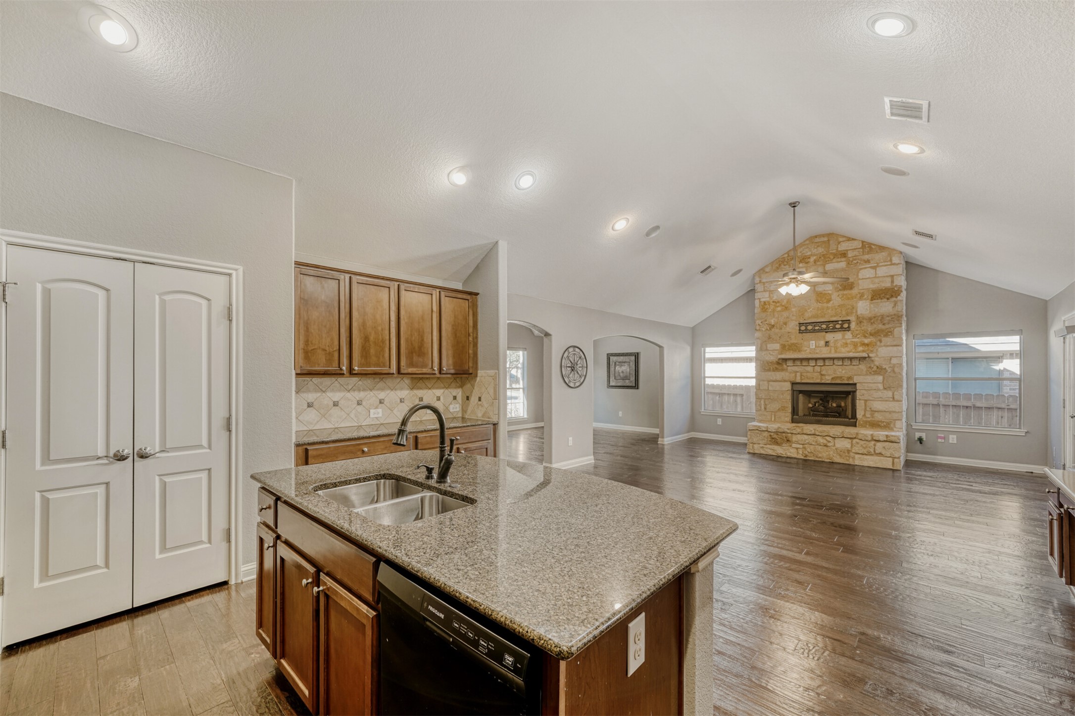2431 Santa Barbara Loop Round Rock, TX 78665 - Photo 14 of 34 Kitchen featuring a kitchen island with sink, brown cabinets, arched walkways, light stone countertops, and dishwasher