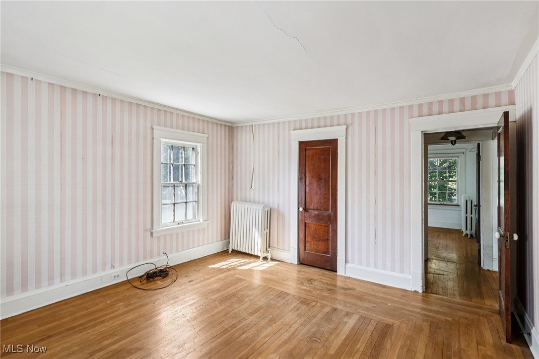 4040 Bayard Road Cleveland, OH 44121 - Photo 42 of 49 Unfurnished room featuring wallpapered walls, wood-type flooring, radiator heating unit, and ornamental molding