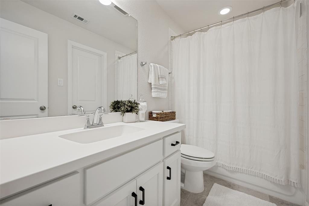 8440 Colburn The Colony, TX 75056 - Photo 20 of 34 Private ensuite bathroom featuring a spacious vanity with quartz countertops, modern cabinetry, and ample storage. The tub/shower combination with tile surround offers both functionality and style, creating a comfortable and convenient bathroom for family members or guests.