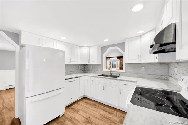 a kitchen with a sink dishwasher a refrigerator and white cabinets with wooden floor