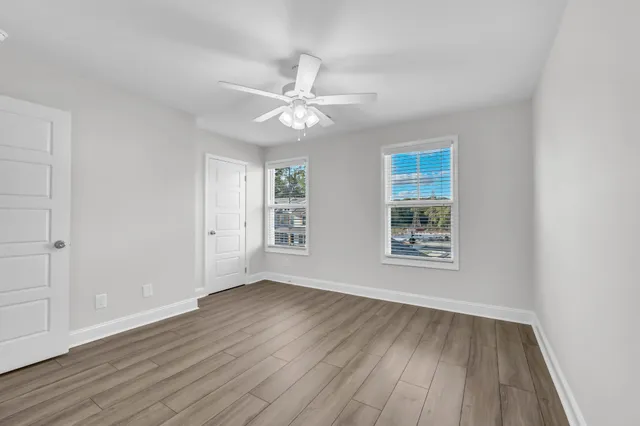 an empty room with wooden floor fan and windows