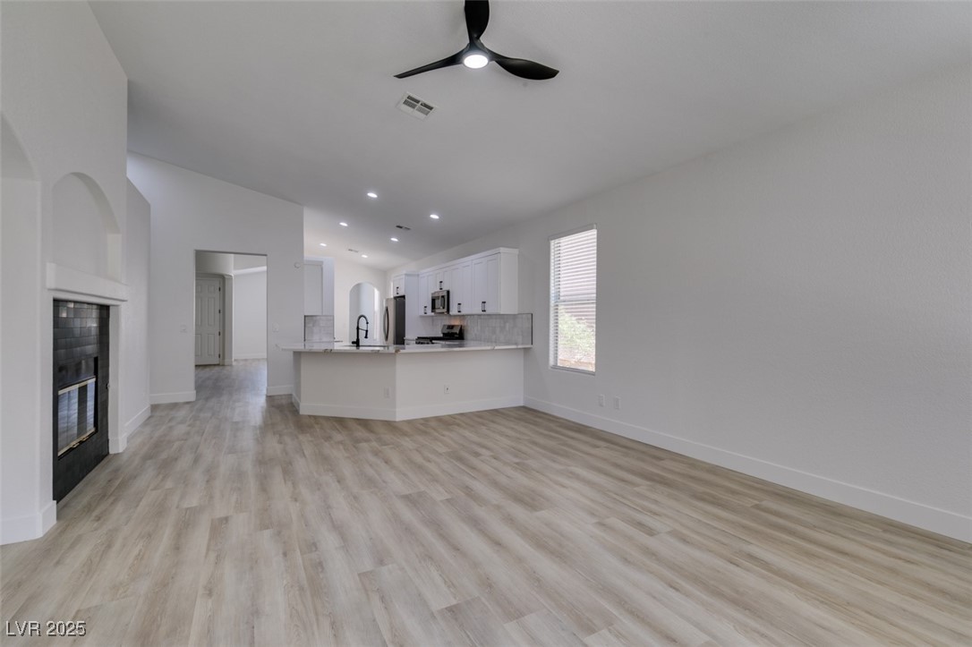 823 Wintersweet Road Henderson, NV 89015 - Photo 22 of 50 Unfurnished living room with a glass covered fireplace, ceiling fan, light wood-style flooring, and recessed lighting