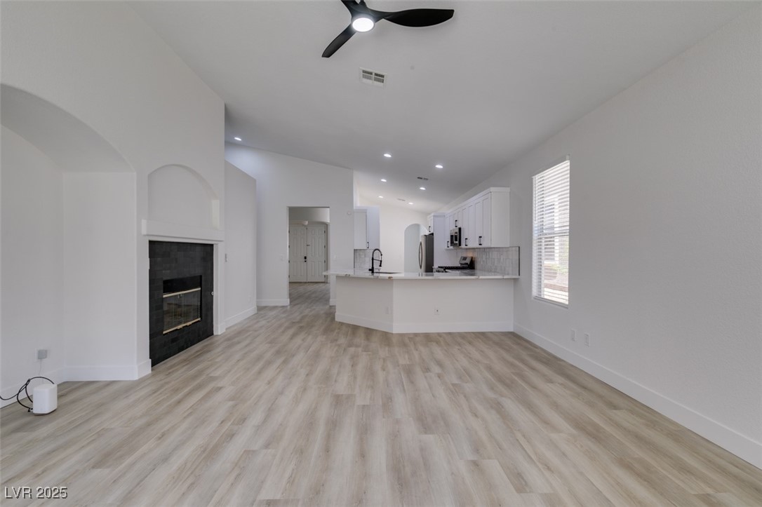 823 Wintersweet Road Henderson, NV 89015 - Photo 23 of 50 Unfurnished living room featuring ceiling fan, light wood-type flooring, arched walkways, a fireplace, and recessed lighting