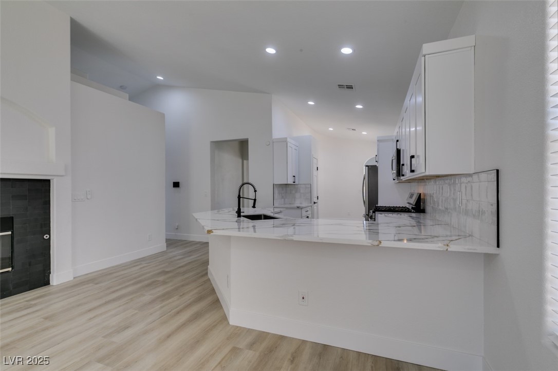 823 Wintersweet Road Henderson, NV 89015 - Photo 26 of 50 Kitchen with white cabinets, light stone countertops, light wood finished floors, backsplash, and appliances with stainless steel finishes