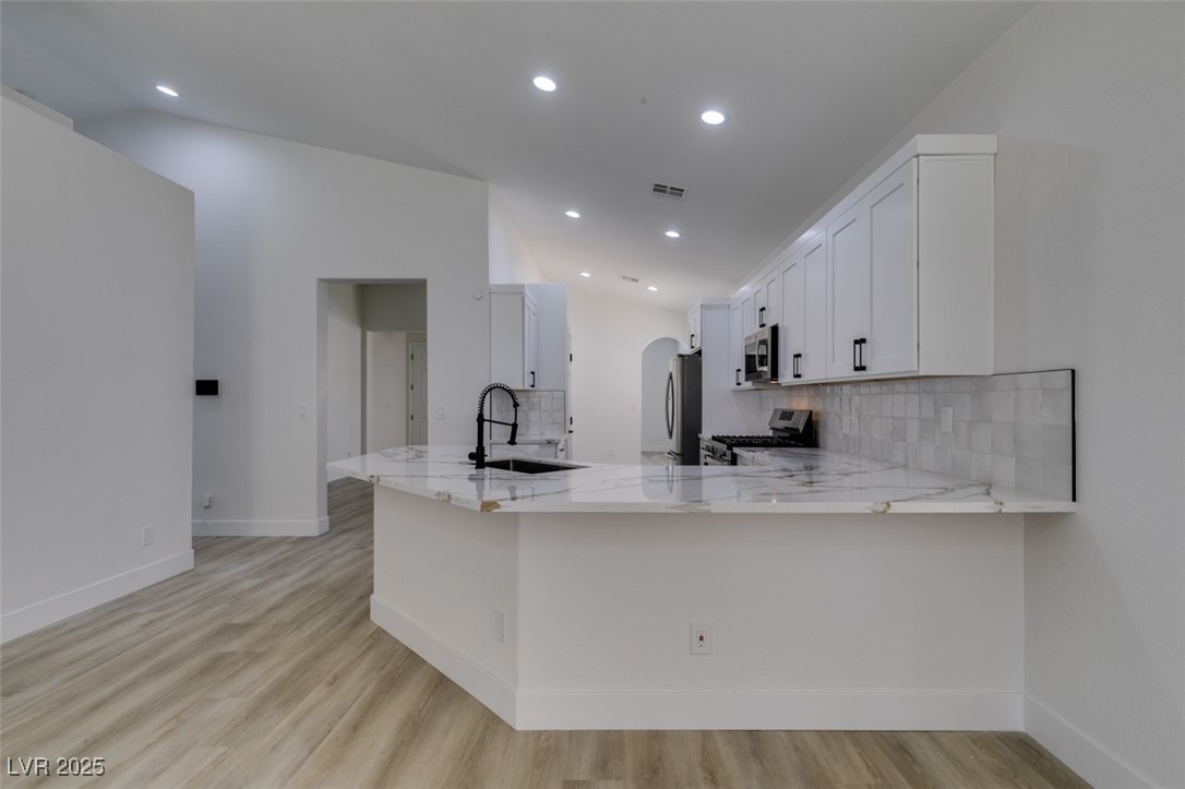 823 Wintersweet Road Henderson, NV 89015 - Photo 27 of 50 Kitchen with tasteful backsplash, white cabinetry, light stone countertops, light wood-type flooring, and arched walkways