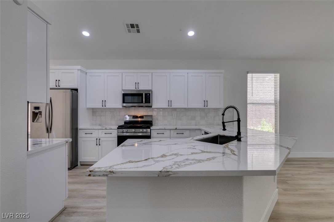 823 Wintersweet Road Henderson, NV 89015 - Photo 29 of 50 Kitchen featuring white cabinetry, appliances with stainless steel finishes, tasteful backsplash, light stone countertops, and light wood-type flooring