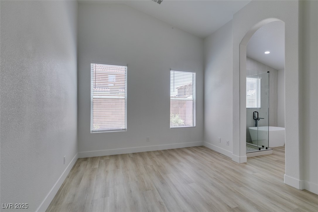 823 Wintersweet Road Henderson, NV 89015 - Photo 38 of 50 Empty room featuring light wood-style floors, arched walkways, and vaulted ceiling