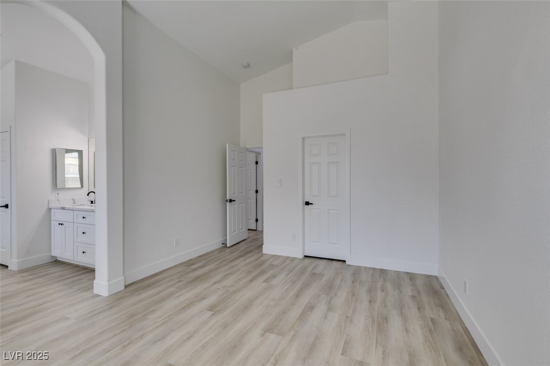 823 Wintersweet Road Henderson, NV 89015 - Photo 40 of 50 Unfurnished bedroom with high vaulted ceiling, light wood-style floors, arched walkways, and connected bathroom