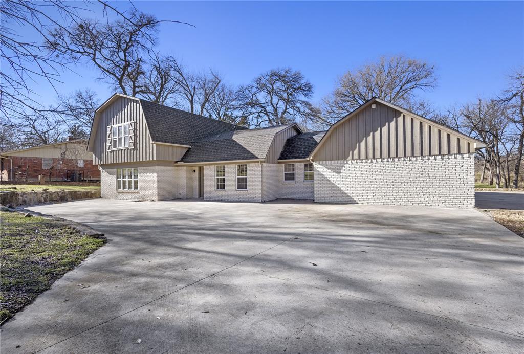View of front of property with driveway, brick siding, roof with shingles, and a gambrel roof