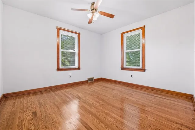 an empty room with wooden floor ceiling fan and windows