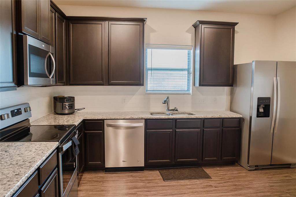 1837 Rialto Lane Crowley, TX 76036 - Photo 14 of 24 Kitchen featuring dark wood cabinetry, light granite-style countertops, a stainless steel appliance suite, white subway tile backsplash, and wood-finish flooring