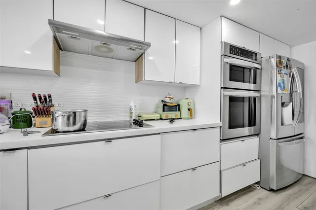 a kitchen with stainless steel appliances granite countertop a refrigerator a stove a sink and white cabinets