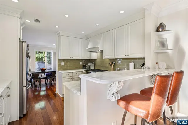 a kitchen with stainless steel appliances granite countertop a stove top oven a sink dishwasher and white cabinets with wooden floor