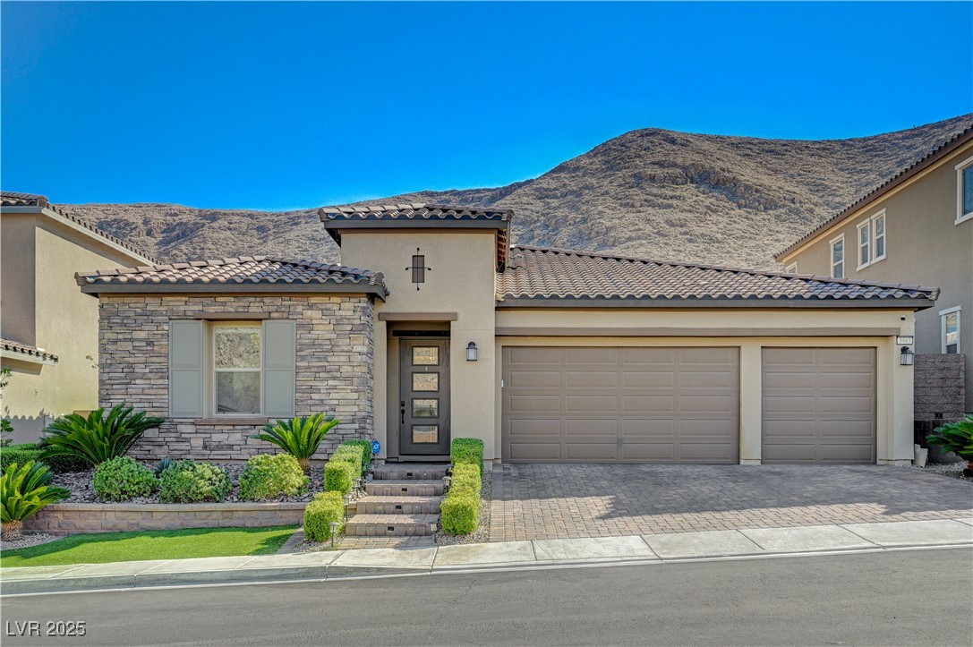 Mediterranean / spanish house with stucco siding, decorative driveway, a garage, stone siding, and a mountain view