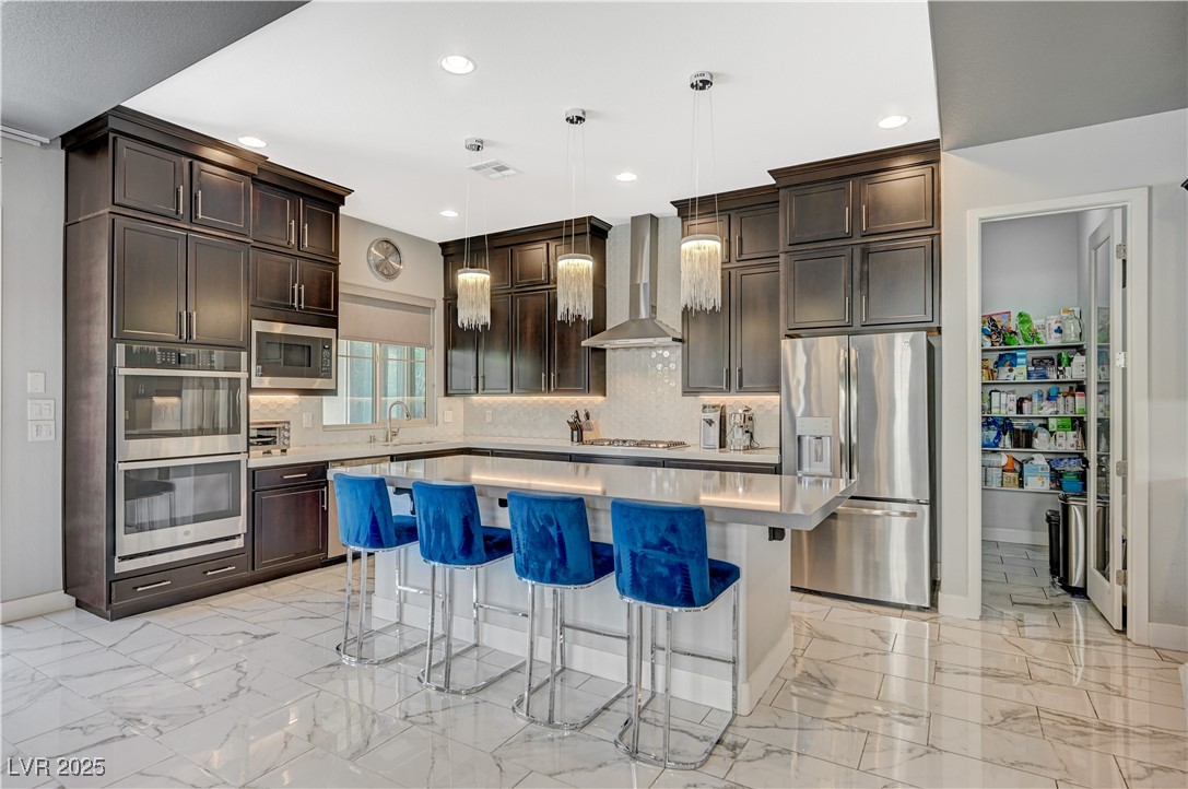 3943 Reyes Avenue Las Vegas, NV 89141 - Photo 14 of 93 Kitchen featuring dark brown cabinetry, hanging light fixtures, a breakfast bar, appliances with stainless steel finishes, and a kitchen island