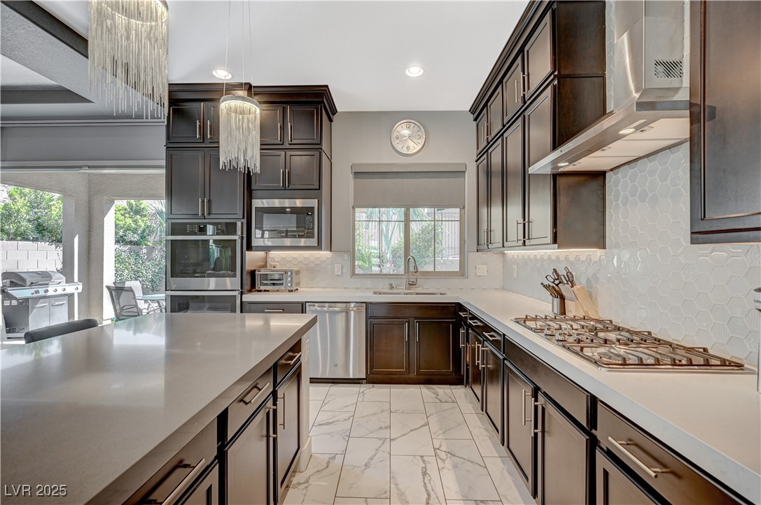 3943 Reyes Avenue Las Vegas, NV 89141 - Photo 16 of 93 Kitchen with tasteful backsplash, dark brown cabinetry, wall chimney range hood, light marble finish floors, and recessed lighting
