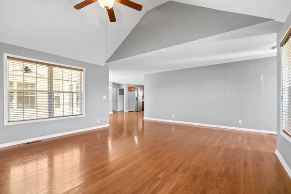 an empty room with wooden floor chandelier fan and windows
