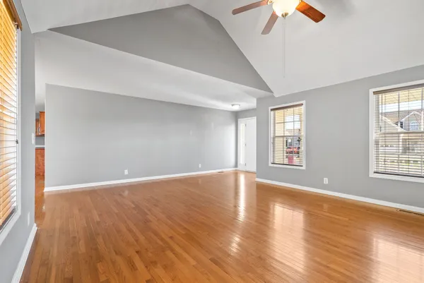 an empty room with wooden floor chandelier fan and windows