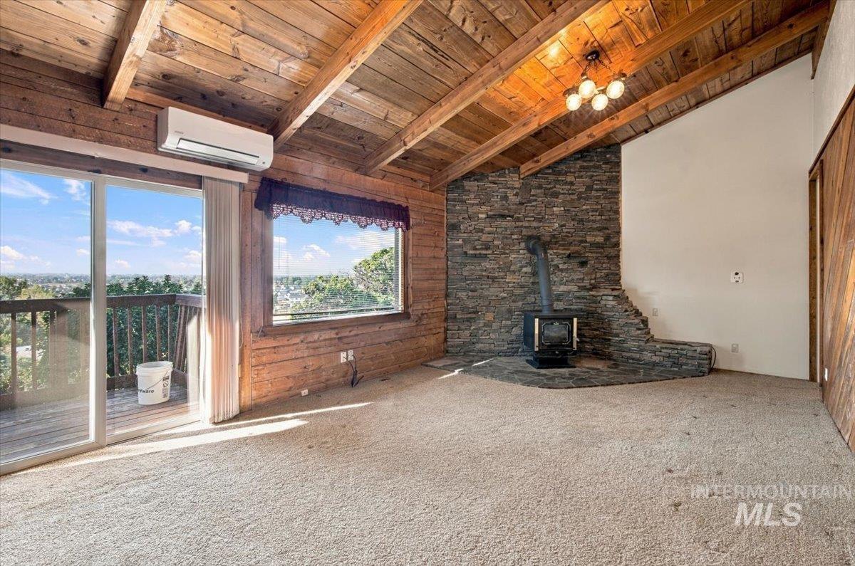 10201 Willis Road Middleton, ID 83644 - Photo 6 of 38 Cathedral wood-paneled ceiling, exposed wood beams, stone accent wall, freestanding wood-burning stove, and sliding glass door to exterior balcony