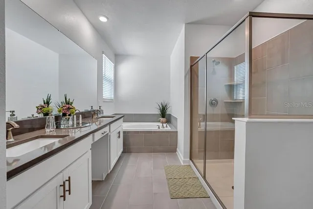 a large white bathroom with a granite countertop double vanity sink a large mirror a bathtub and shower
