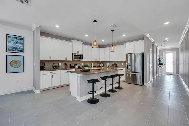 a kitchen with stainless steel appliances kitchen island granite countertop a stove a sink a refrigerator and white cabinets with wooden floor